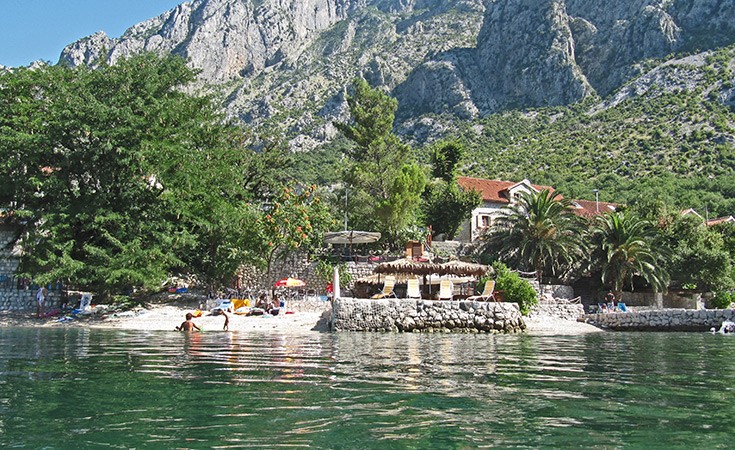 Spiaggia di Orahovac sulla Baia di Kotor interna, riva di ciottoli con il massiccio dell'Orjen attraverso l'acqua, Montenegro